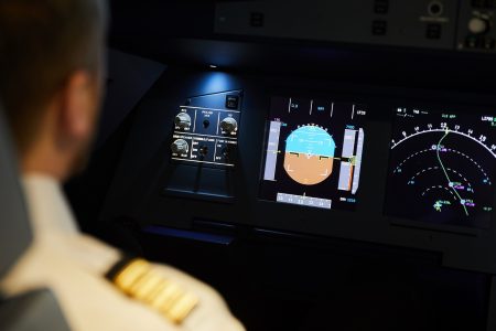 Over shoulder view of pilot sitting at aircraft dashboard with radar meters and planning flight route